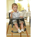 A young child sitting in a Peg-Perego high chair, holding a cookie, in a dining setting.