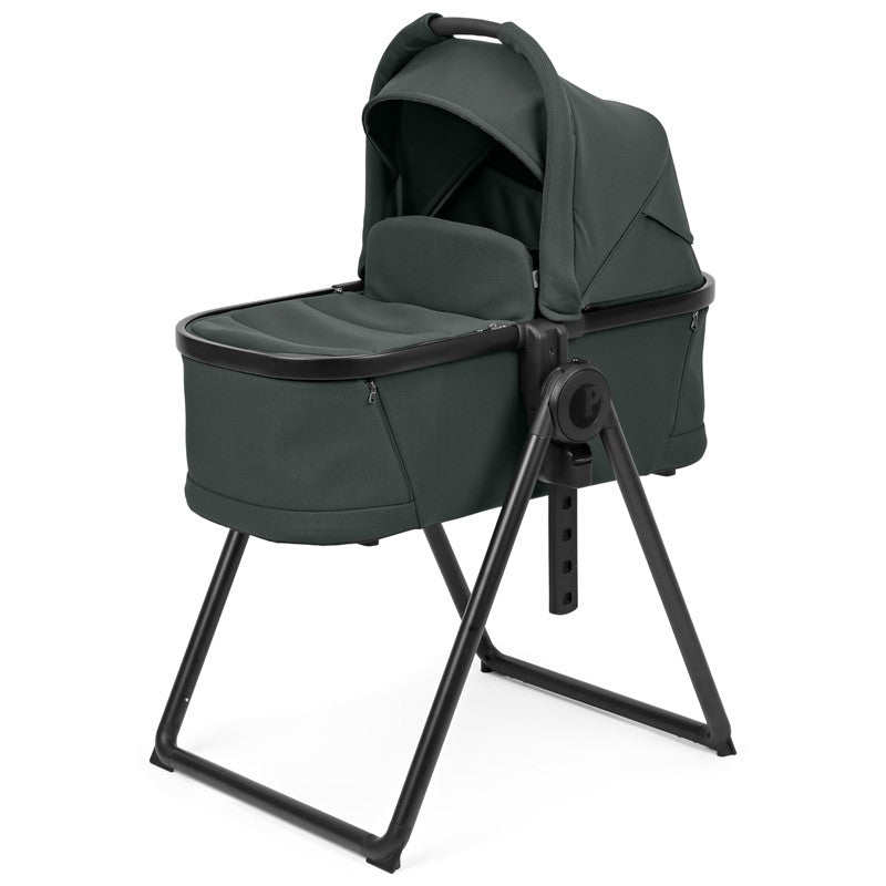 Sage green Peg Perego Ypsi Bassinet with a stand, featuring a soft padded interior and adjustable canopy.