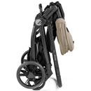 Peg YPSI Single-to-Double Stroller in Vanilla Blend, folded for compact storage, featuring black frame and tan handle.