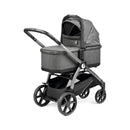 Ypsi Travel System by Peg Perego, featuring a grey fabric stroller with a bassinet, adjustable handle, and modern wheel design.