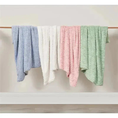Textured faux fur stroller blankets in blue, white, pink, and green hanging on a wooden bar against a neutral wall.