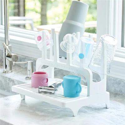 Drying rack for baby bottles, featuring a white design, holding various colored cups and bottles, placed on a countertop.