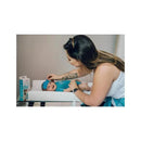 Mother applying a cooling gel patch to a smiling baby lying on a changing table, with the product box visible nearby.