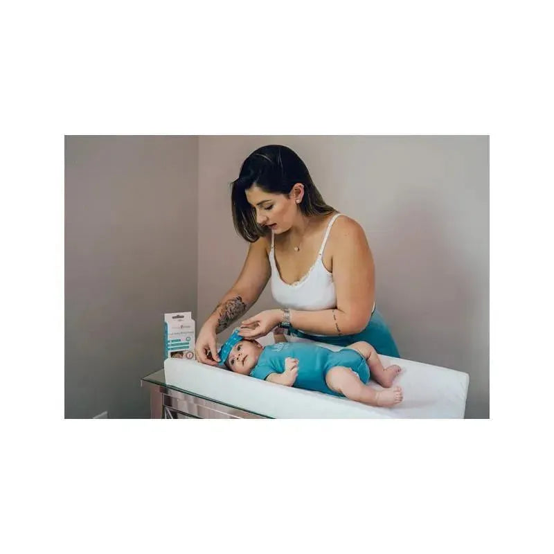 A woman applies a cooling gel patch to a baby lying on a changing table, with a product box visible nearby.