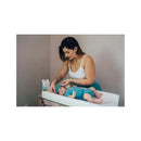 A woman applies a cooling gel patch to a baby lying on a changing table, with a product box visible nearby.
