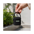 Black Primo Passi bottle bag with dimensions displayed, held by a hand against a blurred outdoor background.