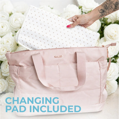 Pink Primo Passi diaper bag with a white polka-dotted changing pad being placed inside, surrounded by flowers.