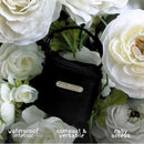 Primo Passi Pacifier Bag in black, featuring a waterproof interior, compact design, and easy access, surrounded by white flowers.