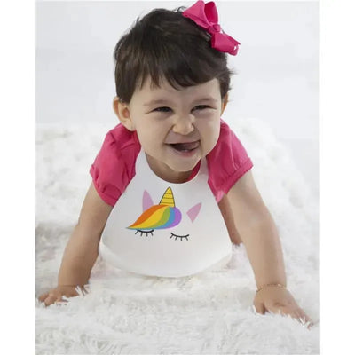 Silicone baby bib featuring a unicorn design, worn by a smiling baby with short hair and a pink shirt.