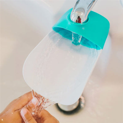 Faucet extender in gumball green is attached to a faucet, directing water flow as a child’s hand holds it.