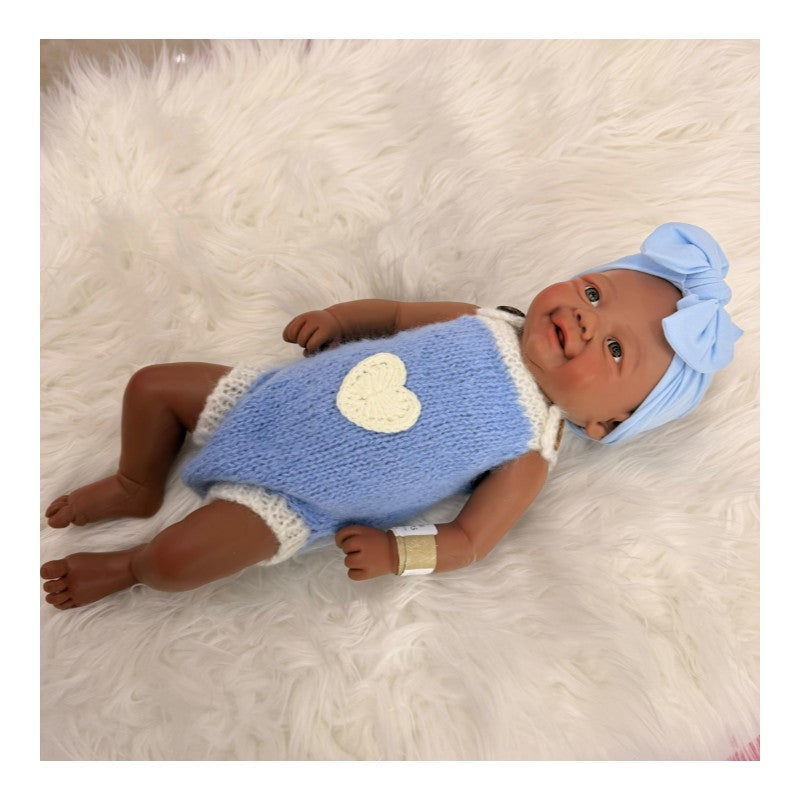 Reborn baby doll with African American features, bald head, wearing a blue outfit with a heart and a matching bow headband.
