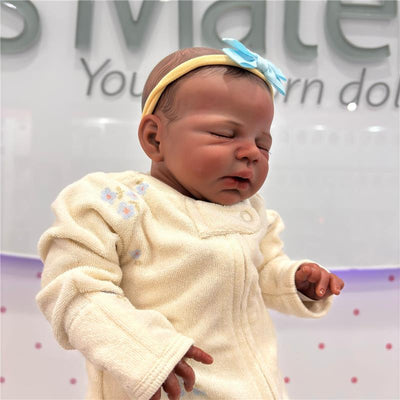 Reborn Baby Doll, African American vinyl, wearing a cream-colored baby outfit with floral designs and a blue hair bow.