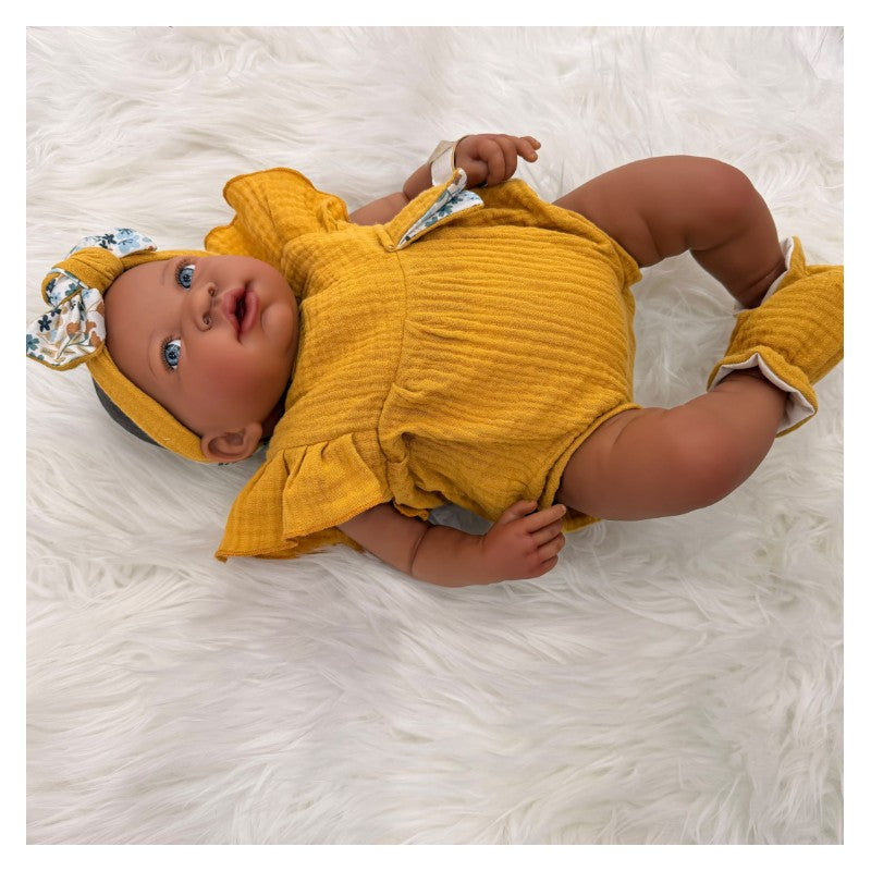 African American reborn baby doll dressed in a yellow outfit with a matching headband and booties, posed on a fluffy white surface.