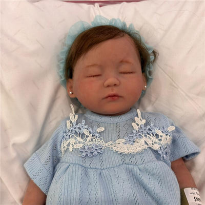Reborn baby doll named Pandora Girl, featuring a full silicone body, closed eyes, blue outfit, and a lace design.