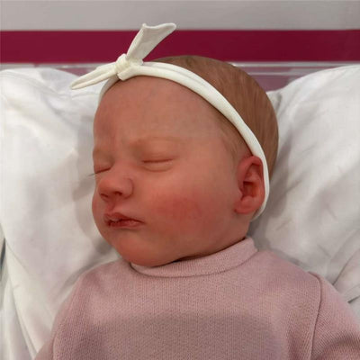 Reborn baby doll named Ashley Asleep, featuring a white vinyl head, realistic facial details, and a pink sweater.