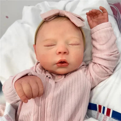 Reborn Baby Doll named Dustin, with closed eyes, wearing a pink outfit and headband, resting on a soft white surface.
