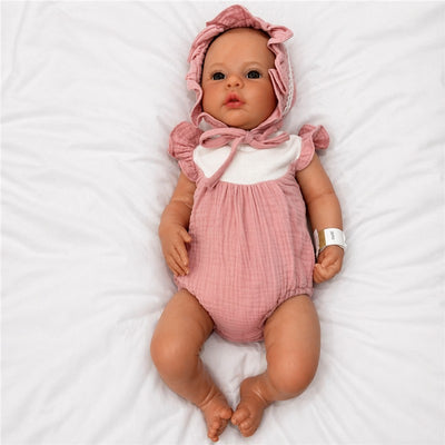 Reborn baby doll named Jocy, with a pink outfit and bonnet, lying on a white surface.