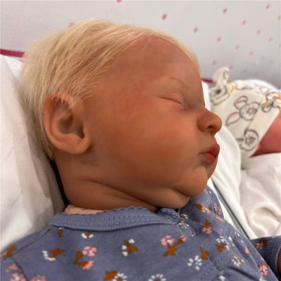 Reborn baby doll named Laura with white vinyl skin and short blond hair, wearing a floral-patterned blue outfit.