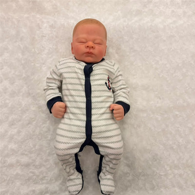 Reborn baby doll Leolonni in a white and navy striped onesie, with a soft facial expression, on a fluffy white background.