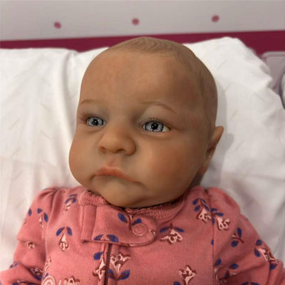 Reborn baby doll featuring white vinyl, open blue eyes, and dressed in a pink floral onesie.