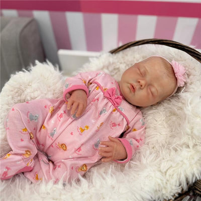 Reborn baby doll wearing a pink outfit with animal prints, resting on a fluffy white blanket in a basket.