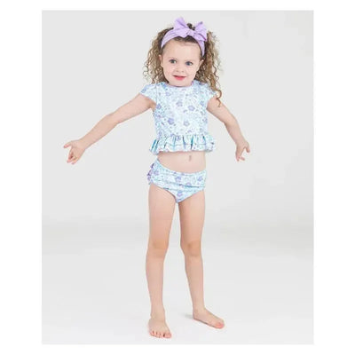 Baby girl wearing a fairytale garden cap sleeve bikini with ruffle hem, styled with a matching lavender headband.