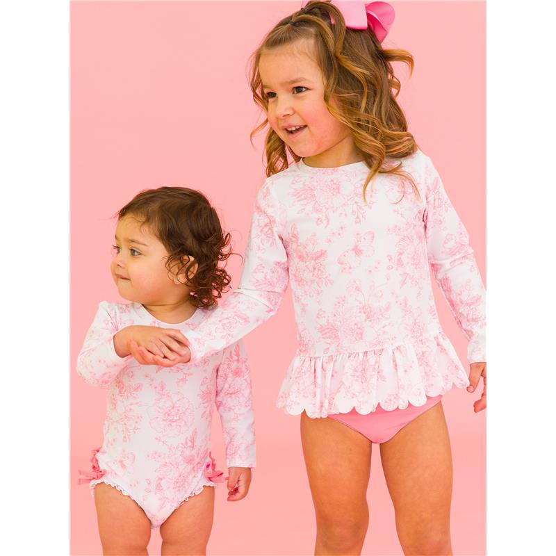Two young girls in matching pink butterfly garden long sleeve swimsuits, one with a ruffled hem, posing against a pink background.