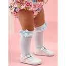 Knee-high socks in light blue with lace and bows, worn by a toddler alongside white shoes and a colorful floral outfit.