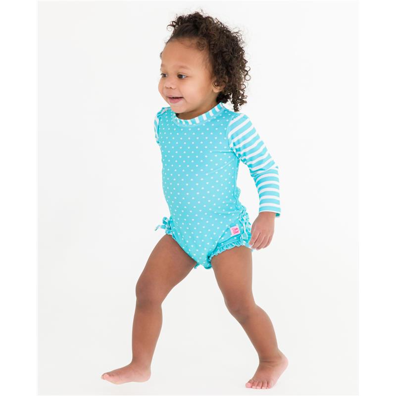 Baby girl wearing an aqua long sleeve rash guard swimsuit with polka dots and striped sleeves, smiling while walking.