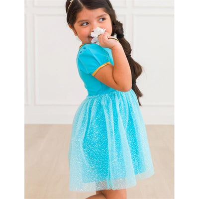 Baby girl in a blue short sleeve bow twirl dress, holding a flower and looking over her shoulder, set against a light background.