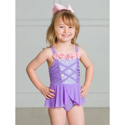 Baby girl modeling a Rufflebutts amethyst one-piece swimsuit with floral accents and a ruffled skirt, smiling cheerfully.