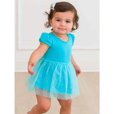 Baby girl wearing a turquoise short-sleeve romper with a glittery tulle skirt and a white bow in her hair, smiling while walking.