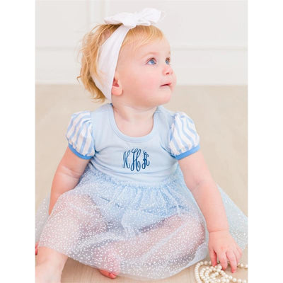 Baby girl wearing a blue and white striped short sleeve romper with a tulle skirt and a large white bow headband, seated and looking up.
