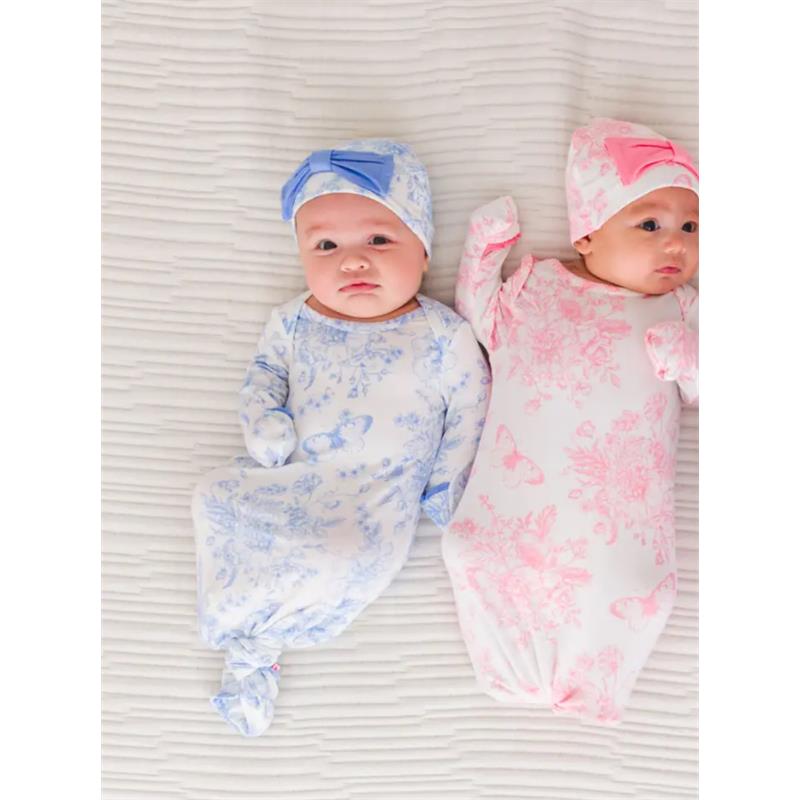Two infants in butterfly-patterned sleep gowns and matching bow hats, one blue and one pink, lying on a textured white surface.