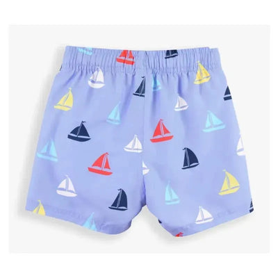 Blue swim trunks featuring a playful sailboat pattern in red, yellow, blue, and white. Ideal for beach or pool wear.