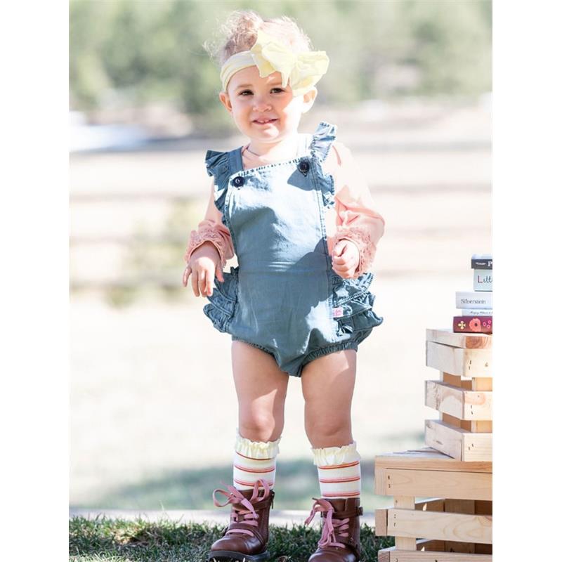 Toddler girl wearing a blue ruffle romper and ivory big bow headband, posed outdoors with playful boots and colorful socks.