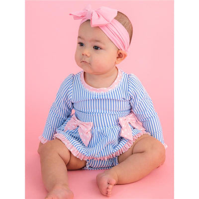 Rufflebutts girls’ periwinkle blue seersucker long sleeve swimsuit with pink bows, worn by an infant sitting against a pink background.