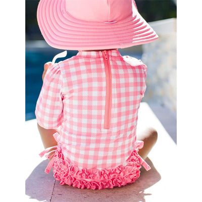 Long sleeve bubblegum pink rash guard with a checkered pattern and ruffled hem, worn by a child.