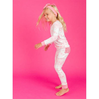 Toddler wearing Rufflebutts bubblegum pink long sleeve pajama set with ruffle details, smiling against a pink background.
