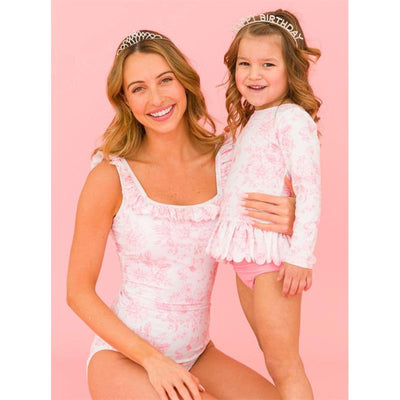 Women and girl model matching bubblegum pink ruffle swimsuits, smiling against a pink background.