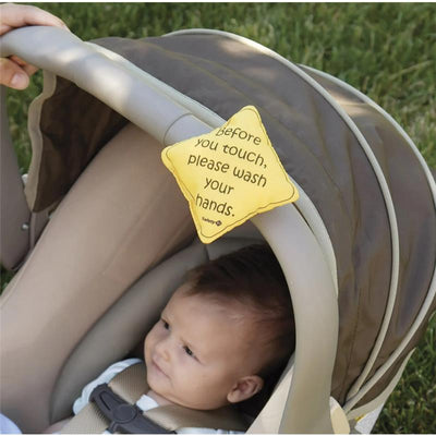 Safety 1st No Germs On Board sign in yellow attached to a stroller, reminding visitors to wash hands before touching the baby inside.