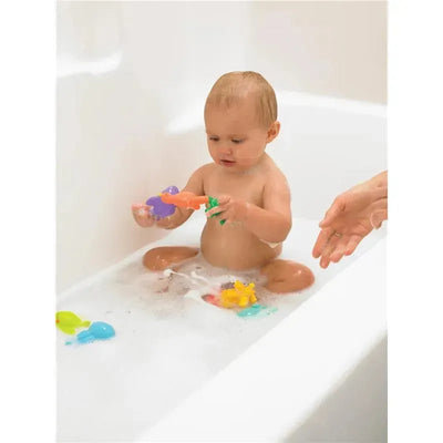 A baby sitting in a bathtub filled with bubbles, playing with colorful sea creature bath toys.