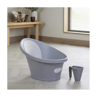 Shnuggle bath rinse jug in Pebble Grey next to a matching ergonomic baby bath, displayed in a bright, modern room setting.