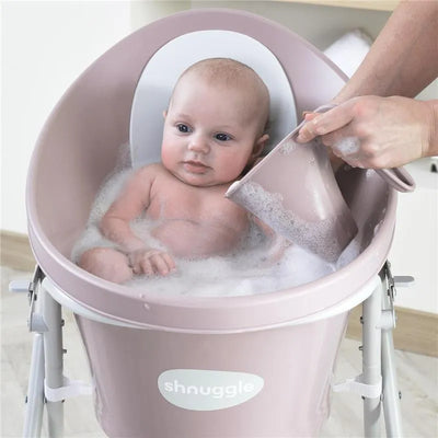 Newborn baby in a Shnuggle bath with bubbles, as an adult gently pours water using a cup.