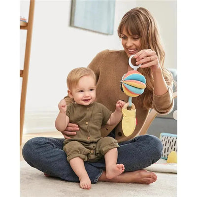 Mother holds a colorful 3-in-1 activity toy while playing with a smiling baby seated on the floor.