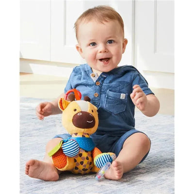 Toddler sitting on a rug with a Skip Hop Bandana Buddies Giraffe stroller toy, smiling and reaching for the toy.