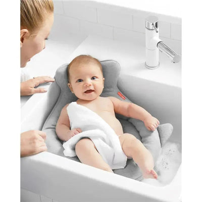 Grey Skip Hop Moby Softspot Sink Bather cradles a smiling baby wrapped in a white towel in a sink.