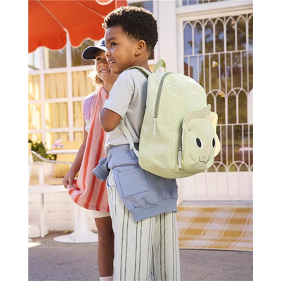 Toddler boy with a green Dino backpack featuring adjustable padded straps, smiling alongside a girl in a striped outfit.