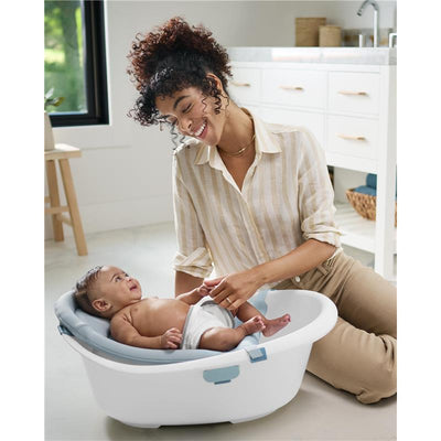 A smiling woman interacts with a happy baby in a Skip Hop Wave 4-In-1 Baby Bath Tub, set in a modern bathroom.