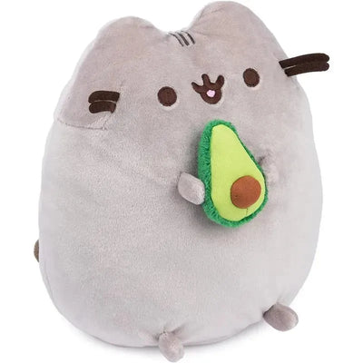Gray plush toy of Pusheen holding a green avocado with a brown pit, suitable for ages 8 and up.
